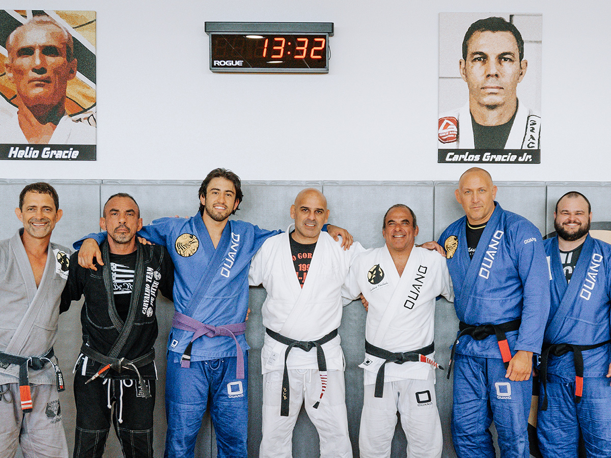 A large group of male professors wearing gis lined up for a photo at Gustavo Machado BJJ Academy.