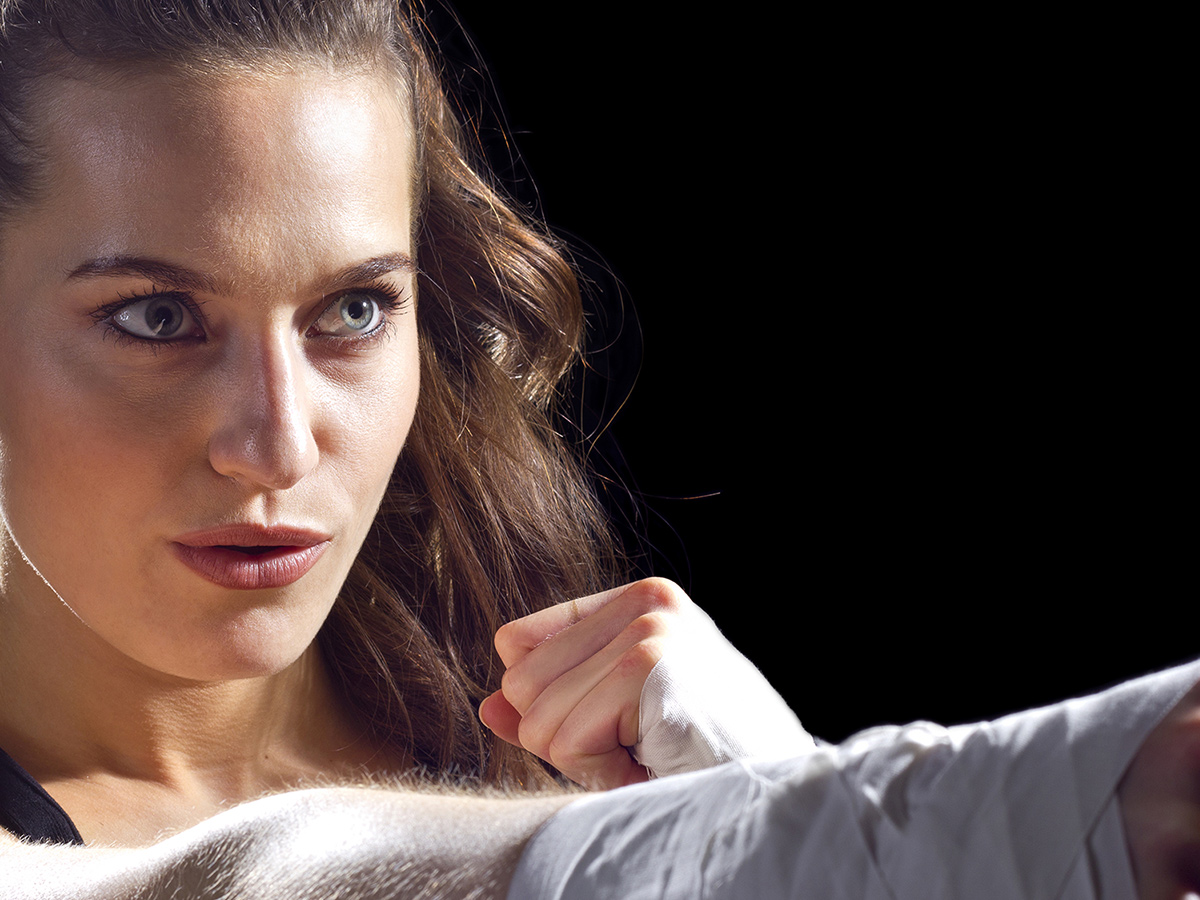 Female MMA fighter with wrapped hands punching on a black background.